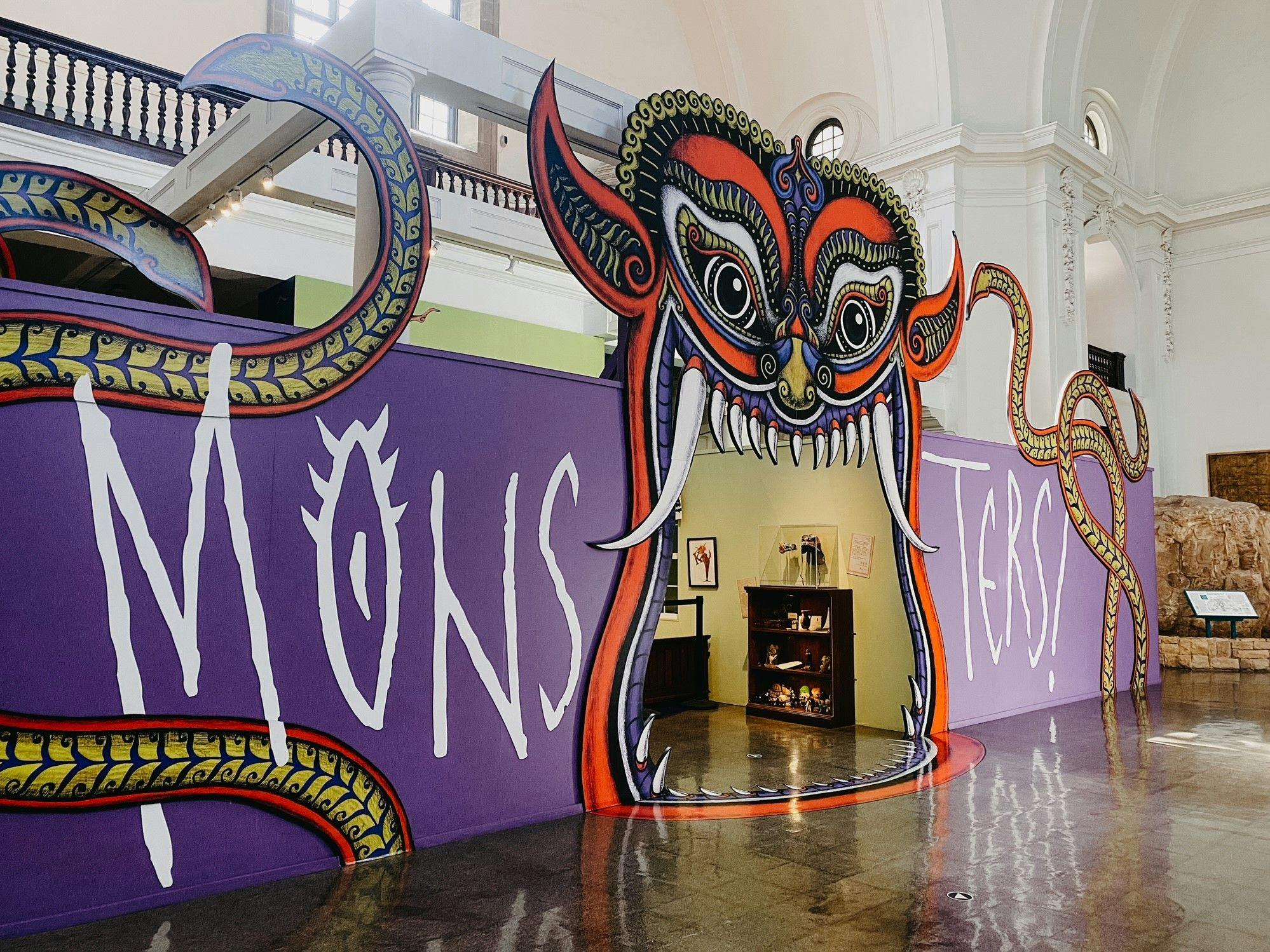 The "Monsters!" exhibit featuring a large wall where a red, demon-like creature's mouth is the exhibit entrance. The exhibit title surrounds it in large, white font.